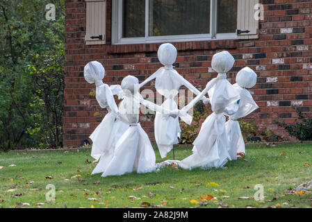 A circle of white clad ghosts play a game of ring around the Rosie as they dance on the lawn of a home decorated for Halloween Stock Photo