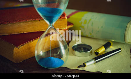 Sand clock with old books and pen with paper map on the wooden table. Concept of travel planning. Stock Photo