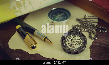 Pocket watch with old books and pen with paper map on the table by the window. Concept of travel planning. Stock Photo