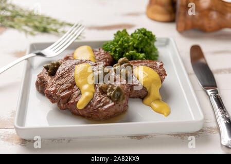 Filet mignon with caper and mustard sauce, broccoli, pepper grinder on wooden white background, soft light Stock Photo