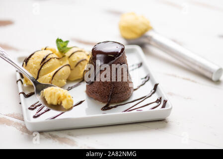 Petit gateau dessert; Petit gateau with vanilla ice cream and chocolate sauce in a white plate on white wooden background. Stock Photo