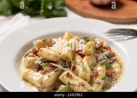 Penne pasta with carbonara sauce in white plate on wooden white background, soft light, angle view. Italian food Stock Photo