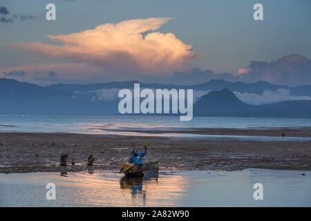 A fisherman pulls his net into his cayuco at sunset on Lake Atitlan, Guatemala.  In the background is Cerro del Oro and the east shore of the lake . Stock Photo