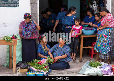 Several women of mixed ages in the typical native dress of San Antonio Palopó, Guatemala, sell vegetables at the small local market on the street. Stock Photo