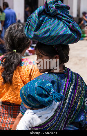 A young Mayan woman in the traditional dress of San Antonio Palopó, Guatemala, carries her baby on her back in a tzute or utility cloth. Stock Photo