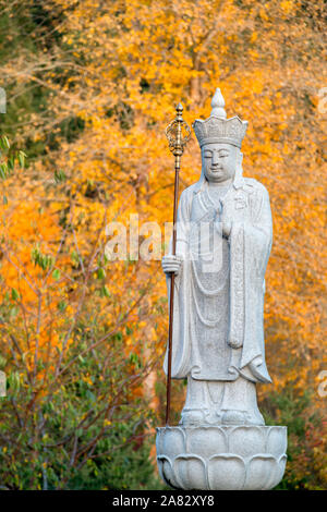 Ksitigarbha Buddha, a Bodhisattva, stone statue with yellow fall colors in the background Stock Photo