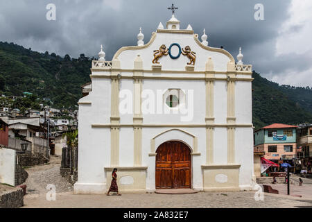 A young Mayan woman in traditional dress walks in front of the Church of Santa Catarina Palopo in Guatemala. Stock Photo