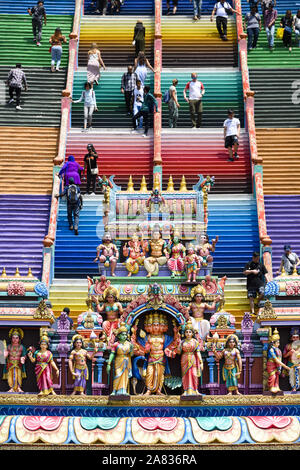 (Selective focus) Representation of Hindu gods and tourists climbing a colorful stairs leading to the Batu Caves Stock Photo