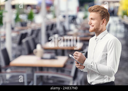 Handsome waiter with notebook in outdoor cafe Stock Photo