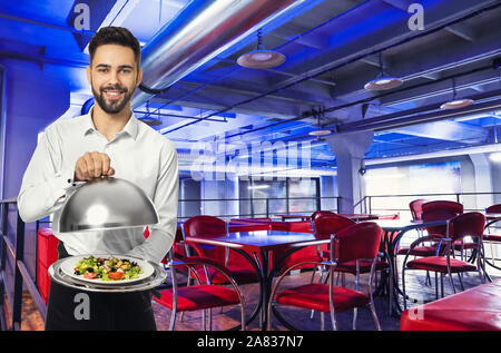 Handsome waiter with fresh salad in modern cafe Stock Photo