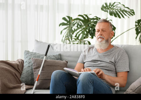 Blind mature man reading book written in Braille at home Stock Photo