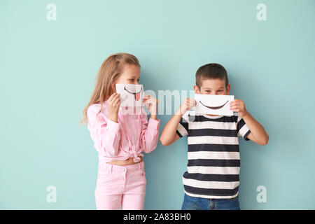 Little children hiding mouths behind drawn smiles on color background Stock Photo