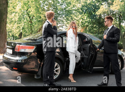 Young celebrity getting out of car surrounded by bodyguards Stock Photo