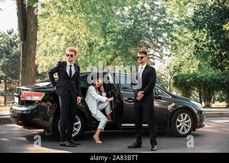 Young celebrity getting out of car surrounded by bodyguards Stock Photo