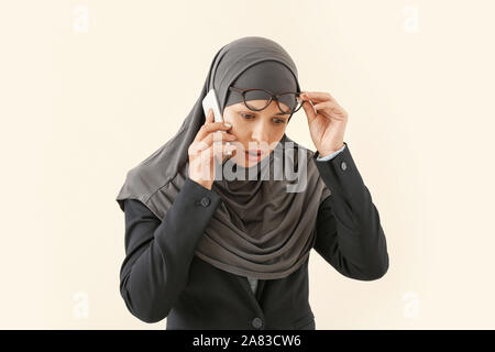Portrait of Muslim woman talking by mobile phone on light background Stock Photo