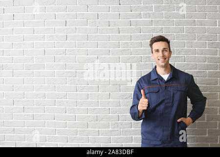 Male car mechanic showing thumb-up near brick wall Stock Photo