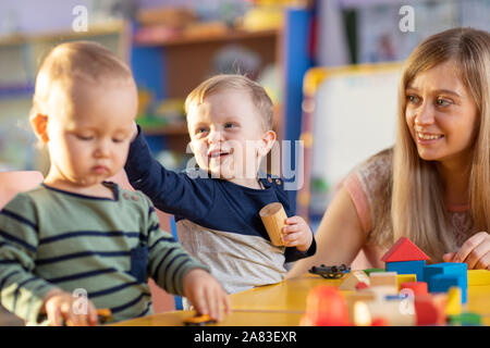 Young teacher and kids toddlers playing with building blocks toy at kindergarten Stock Photo