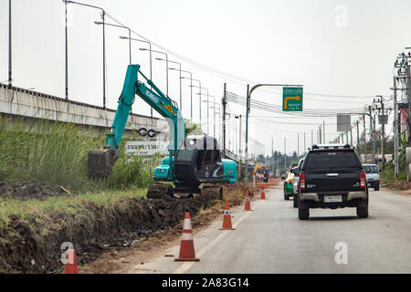 SAMUT PRAKAN, THAILAND, APR 27 2019, Excavator working beside a road. Digger digs pit along roadway. Stock Photo