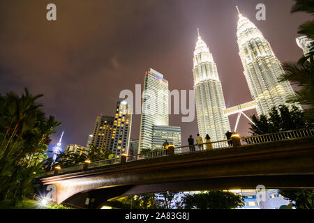 KL Tower and the Petronas Twin Tower illuminated at dusk. People enjoying the view from a bridge in KLCC Park Stock Photo