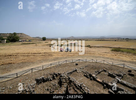 Remains of buildings in front of the Nuraghe Santu Antine near Sassari in Sardinia and the surrounding countryside with a tractor at work Stock Photo