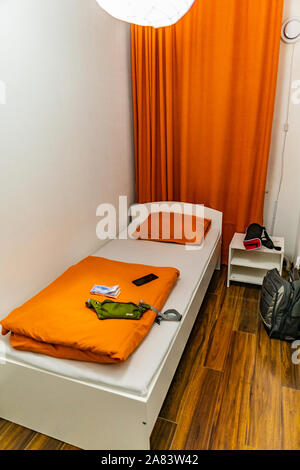 Hostel Simple Single Bed Room with Orange Colored Curtain Linen and Modest Cubicle Stock Photo