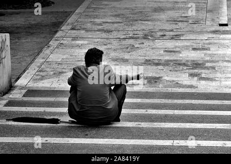 Poor man begging for help on the street/ Homeless beggar man sitting outdoors in city asking for money donation Stock Photo