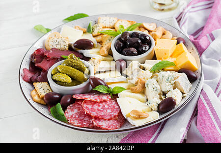 Antipasto platter with basturma, salami, blue cheese, nuts, pickles and olives on a white wooden background. Stock Photo