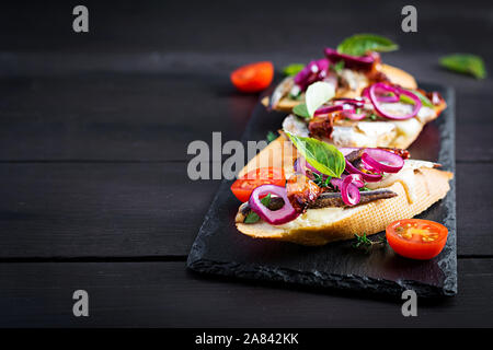 Tapas - Spanish bar food. Bruschetta with slices of sun-dried tomatoes,cheese mozzarella and anchovies on dark background. Stock Photo