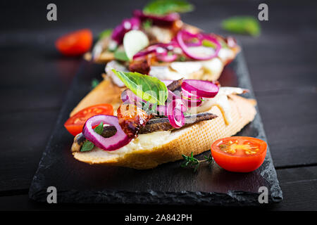 Tapas - Spanish bar food. Bruschetta with slices of sun-dried tomatoes,cheese mozzarella and anchovies on dark background. Stock Photo