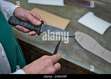 Craftsman's hands sharpening the edge of the cutter with a knife whetstone to better cut the tool. Stock Photo