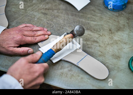 Hands of an orthopedic artisan sticking with the help of a blue wooden mallet some foam templates and handmade rubber and personlaized for the feet. Stock Photo