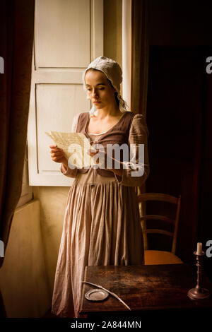 Vermeer style portrait of a young maid in renaissance costume reading a letter at her window Stock Photo