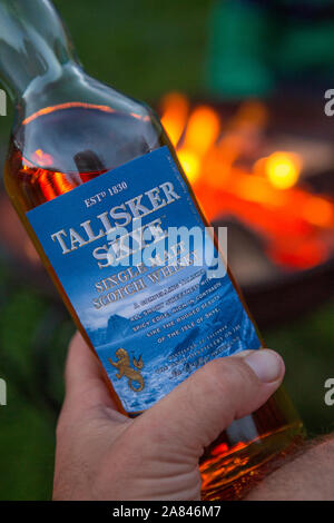 A close up of a bottle of Talisker Skye whiskey being held in front of a camp fire. Stock Photo