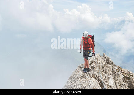 Man on a narrow mountain ridge surrounded by fog, up on via ferrata Eterna (Cadore Brigade) at Marmolada, Dolomites mountain range, Italy.  Copy space Stock Photo