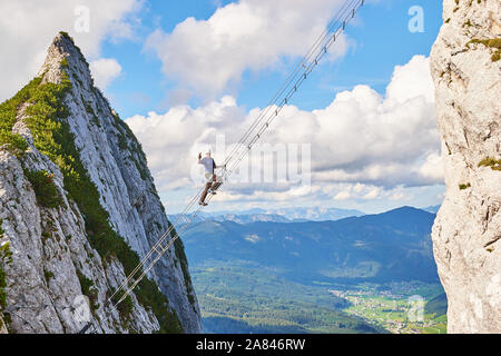 Intersport Donnerkogel via ferrata in Summer, with a man showing a victory sign while climbing the diagonal ladder. Stairway to heaven concept. Stock Photo