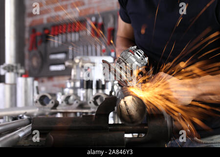 hands man work in home workshop garage with angle grinder, sanding metal makes sparks closeup, diy and craft concept Stock Photo