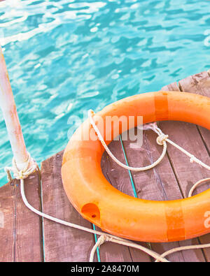 Orange lifebuoy with rope on a wooden pier near sea. Close up of lifebuoy on wooden pier at the beach. Stock Photo