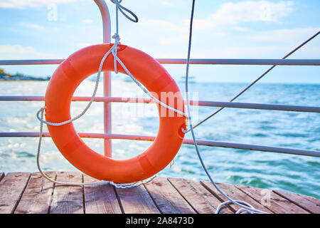 Orange lifebuoy with rope on a wooden pier near sea. Close up of lifebuoy on wooden pier at the beach. Stock Photo