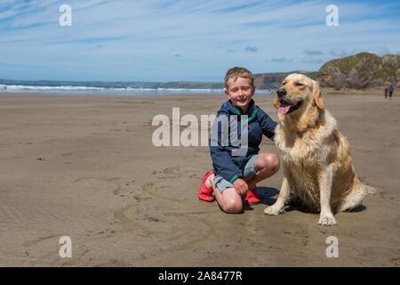 A young boy standing on an empty beach with his pet golden retriever. Stock Photo