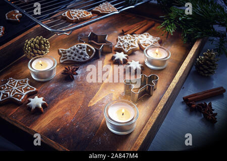 Burning candles, gingerbread and cookie cutters on a dark wooden tray, Christmas arrangement, selected focus, very narrow depth of field Stock Photo