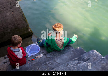 Two boys crabbing on the side of a harbour wall. Stock Photo