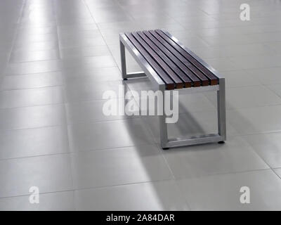 Bench with white metal steel frame and wooden seat elements on the grey tile floor and with cool lighting Stock Photo