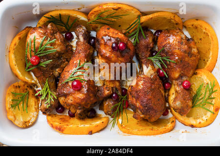 Baked chicken drumstick with oranges and cranberries in a baking sheet on a wooden background. Christmas food Close up. Stock Photo