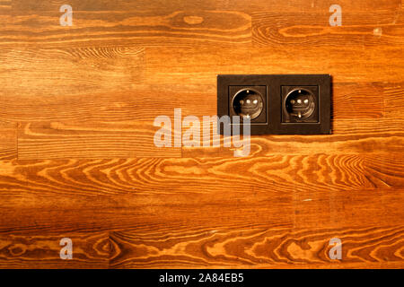 Black power outlet on brown varnished wood wall. Stock Photo