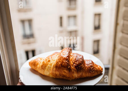 Morning fragrant crispy breakfast croissant on a plate in the opening of an open window