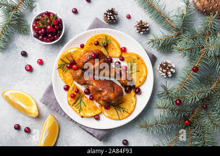 Baked chicken drumstick with oranges and cranberries in a plate light grey background. Christmas food Table with decorations Stock Photo