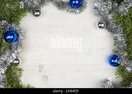 Christmas copy space with pine branches, silver garland and silver and blue Christmas baubles on a light wooden background Stock Photo