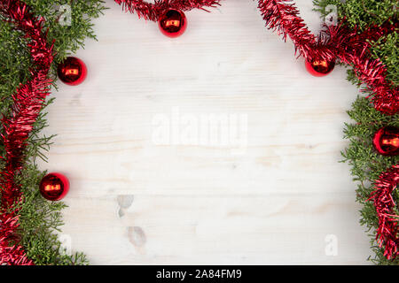 Christmas copy space with pine branches, red garland and red Christmas baubles on a light wooden background Stock Photo