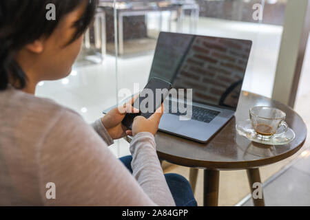 Woman working on laptop and using cellphone at coffee table Stock Photo