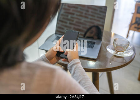 Asian woman using smartphone and laptop at coffee table Stock Photo